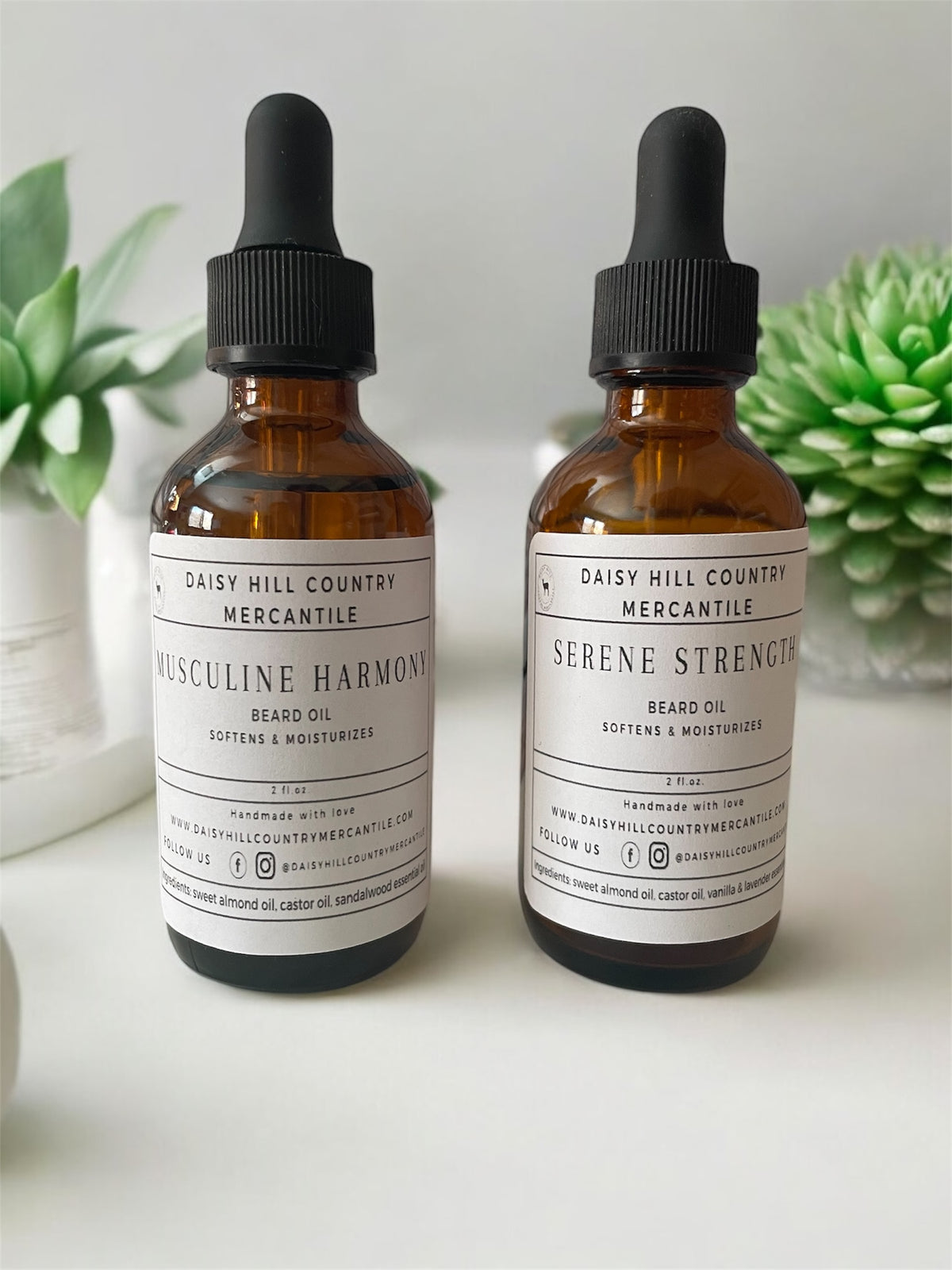 Two amber glass dropper bottles labeled 'BEARD OIL' with different scents, placed on a white surface with a green plant in the background.