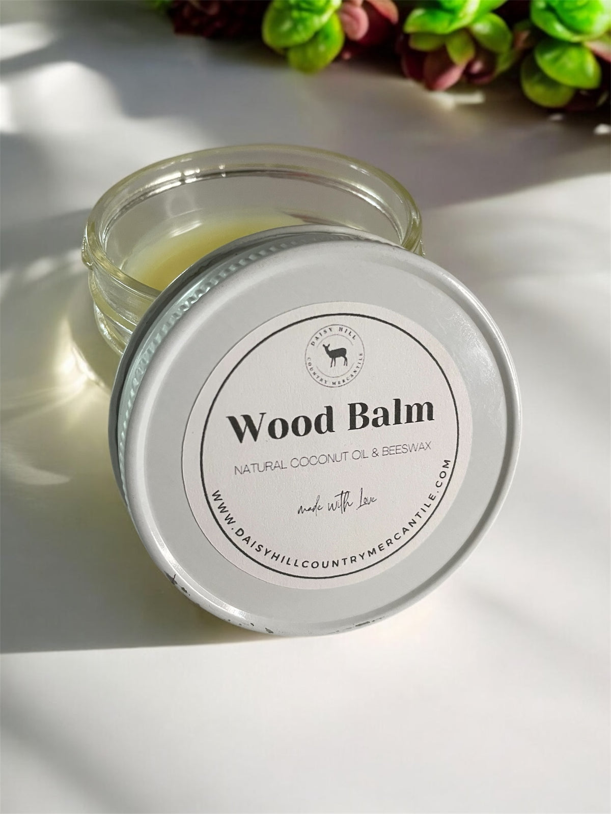A 4 oz glass jar of Natural Wood Balm, placed on a wooden surface with a bright background.