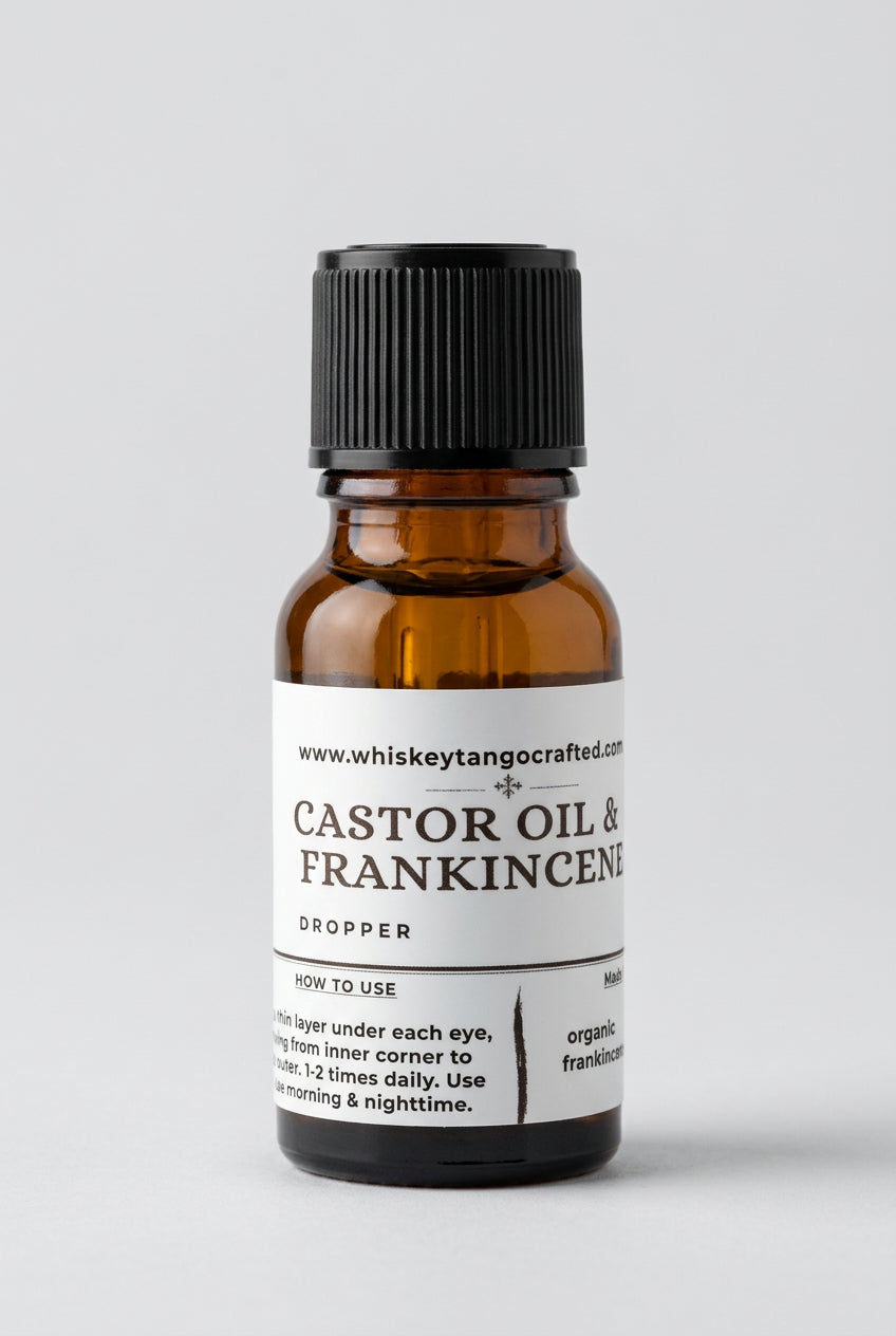 A small amber glass dropper bottle of Whiskey Tangs Castor Oil & Frankincense with a black cap and a beige label, set against a neutral light gray background.